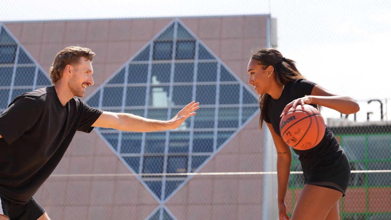 A man and a woman playing basketball. They're both smiling while the woman holds the ball.