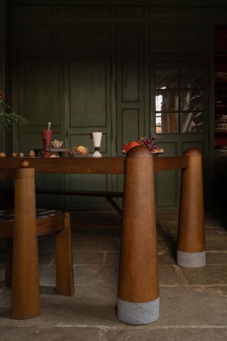 Close-up of flared-leg wood dining table against moss green panelled wall