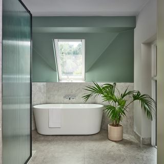 a bathroom with a bathtub, a reeded shower screen and green walls