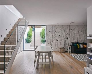 A white basement with glass staircase railing, light wooden flooring and white dining area with white walls and feature wall decor