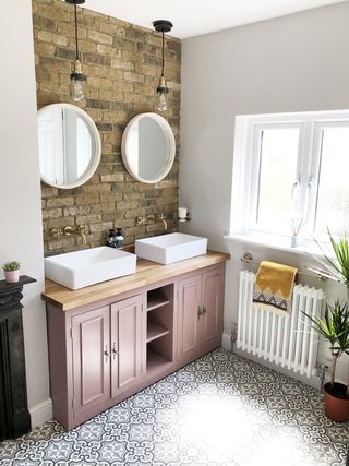 Couples bathroom with exposed brick wall, pink units and patterned motif floor tiling