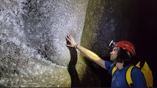 Screenshot from a video showing a researcher touching the world's largest spiderweb.