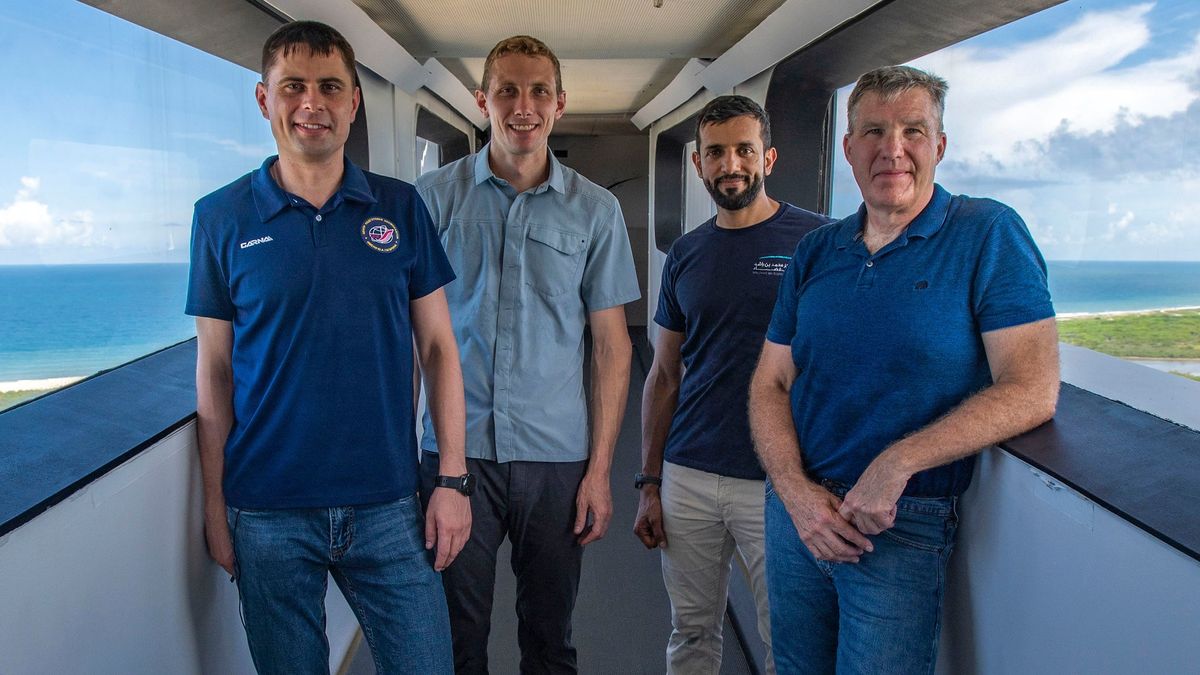 four astronauts inside of a launch tower tunnel with views of the ocean behind them