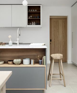 Grey and white kitchen ideas with white cabinets, a grey, wood and white island, and pale wood stool and door