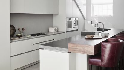 A modern kitchen with white, matt lacquer, handleless cabinetry and black walnut raised breakfast bar 