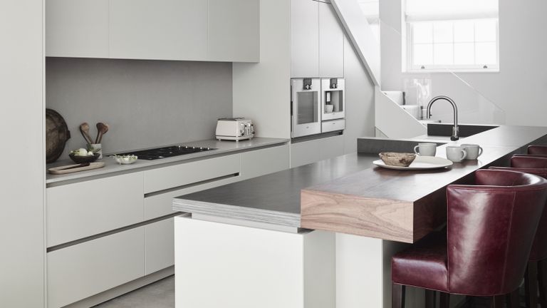 A modern kitchen with white, matt lacquer, handleless cabinetry and black walnut raised breakfast bar