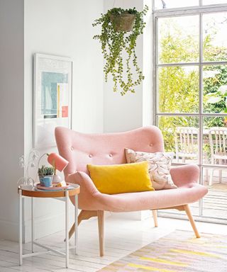Large pink armchair in corner of home office with white side table beside and plant hanging from ceiling