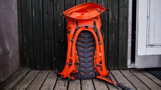 A bright orange Salewa Ortles Wall 38L Backpack rests against a wooden outer wall.