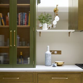 Green and gold kitchen with bookshelves behind ribbed glass doors