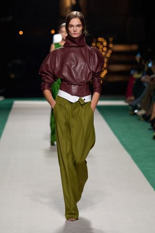 Modelo desfilando na passarela de Victoria Beckham vestindo calça verde.