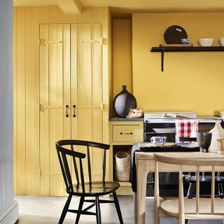 Bright yellow kitchen with wall panelling, wooden table and black chair