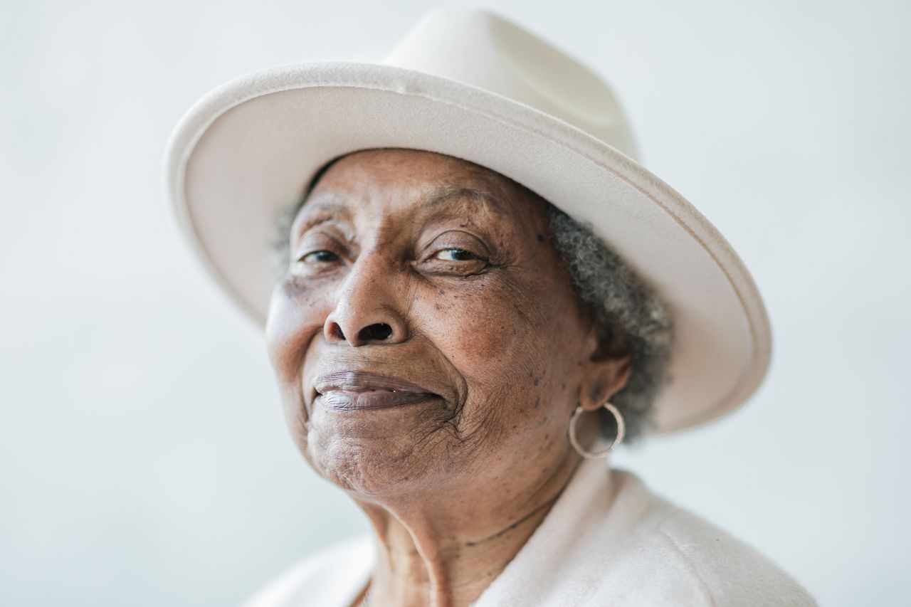 Portrait of an older woman wearing a white hat and smiling.