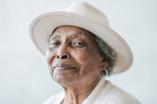 Portrait of an older woman wearing a white hat and smiling.