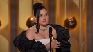 Lily Gladstone talking into a mic and holding her Golden Globe.