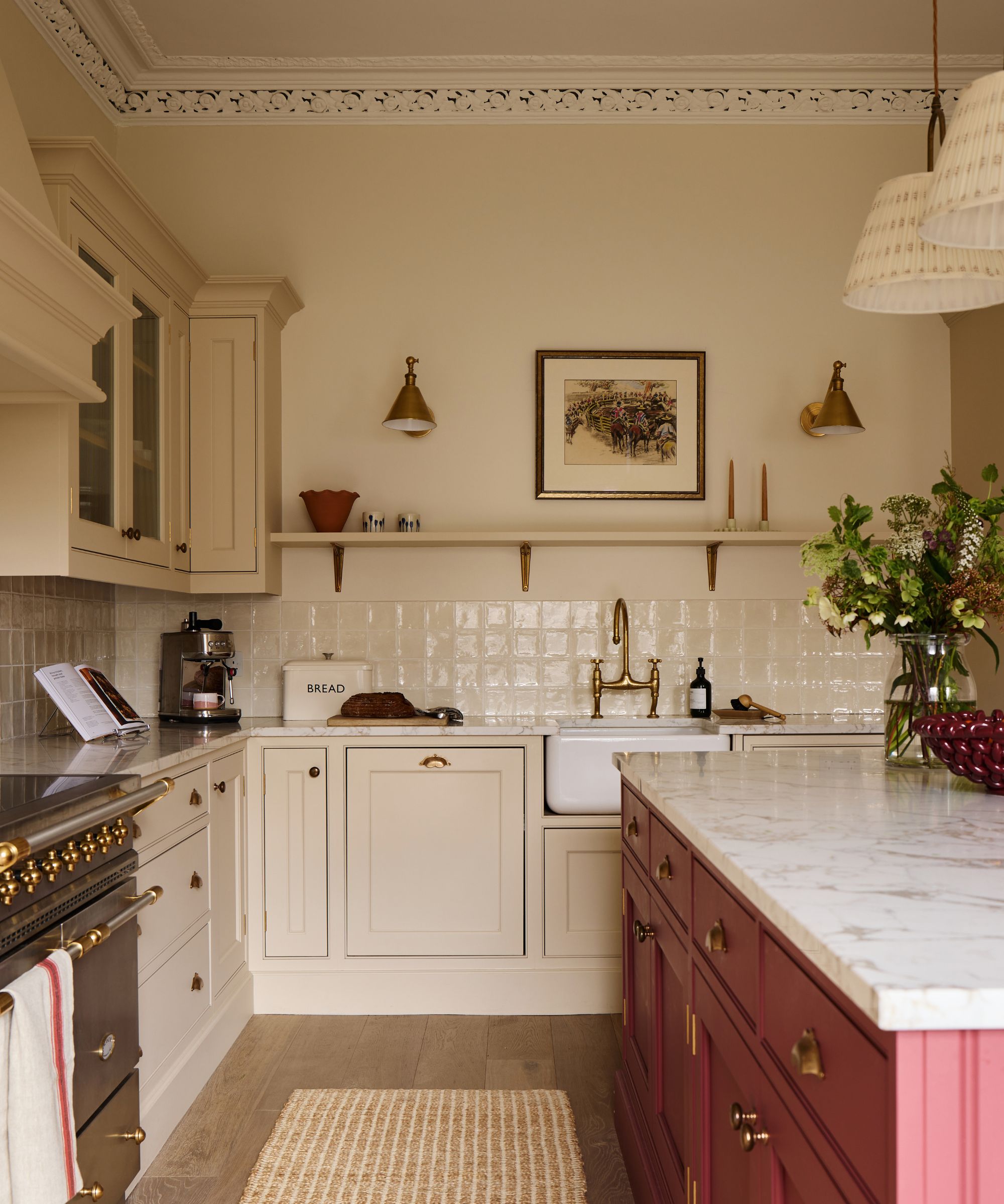 Classic kitchen with cream cabinets, white tile backsplash, brass fixtures, and a rich cranberry-red island topped with white marble