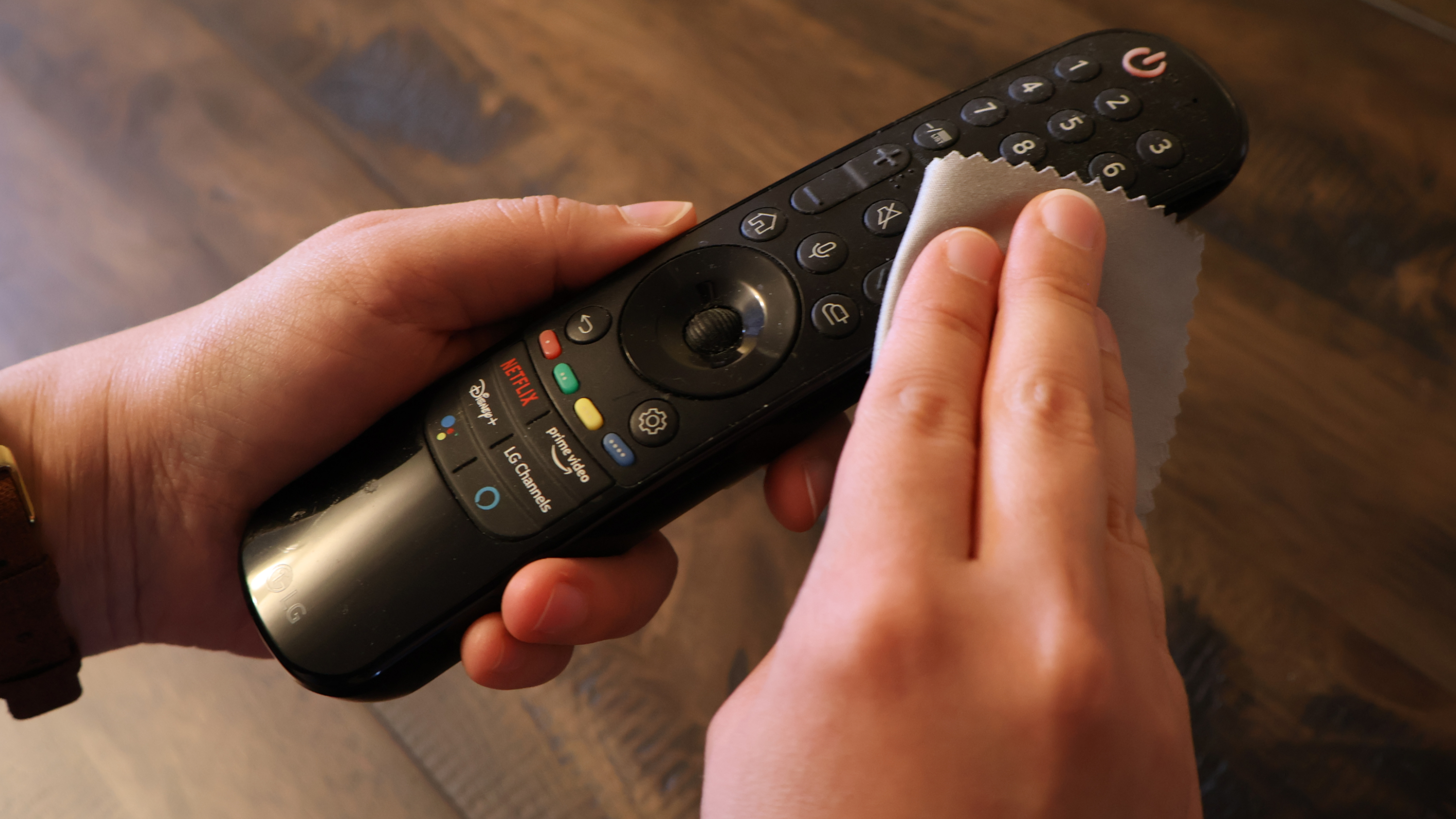 A pair of hands wiping down an LG-branded TV remote with a slightly damp microfiber cloth