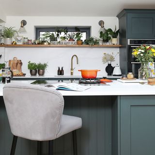 kitchen with brass tap and granite sink with orange casserole dish and open shelf by a window