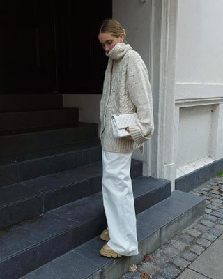 The woman is wearing a knitted scarf, white jeans and beige boots.