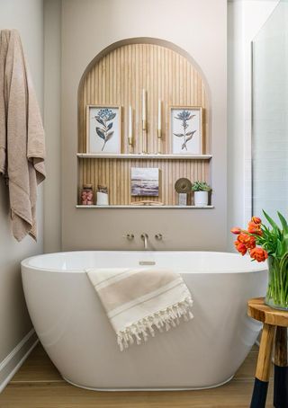 Warm neutral bathroom with roll top tub and tulips on a stool in front of screened shower