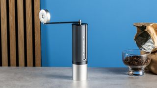 the aeropress manual coffee grinder in gray and silver against the tom's guide blue background