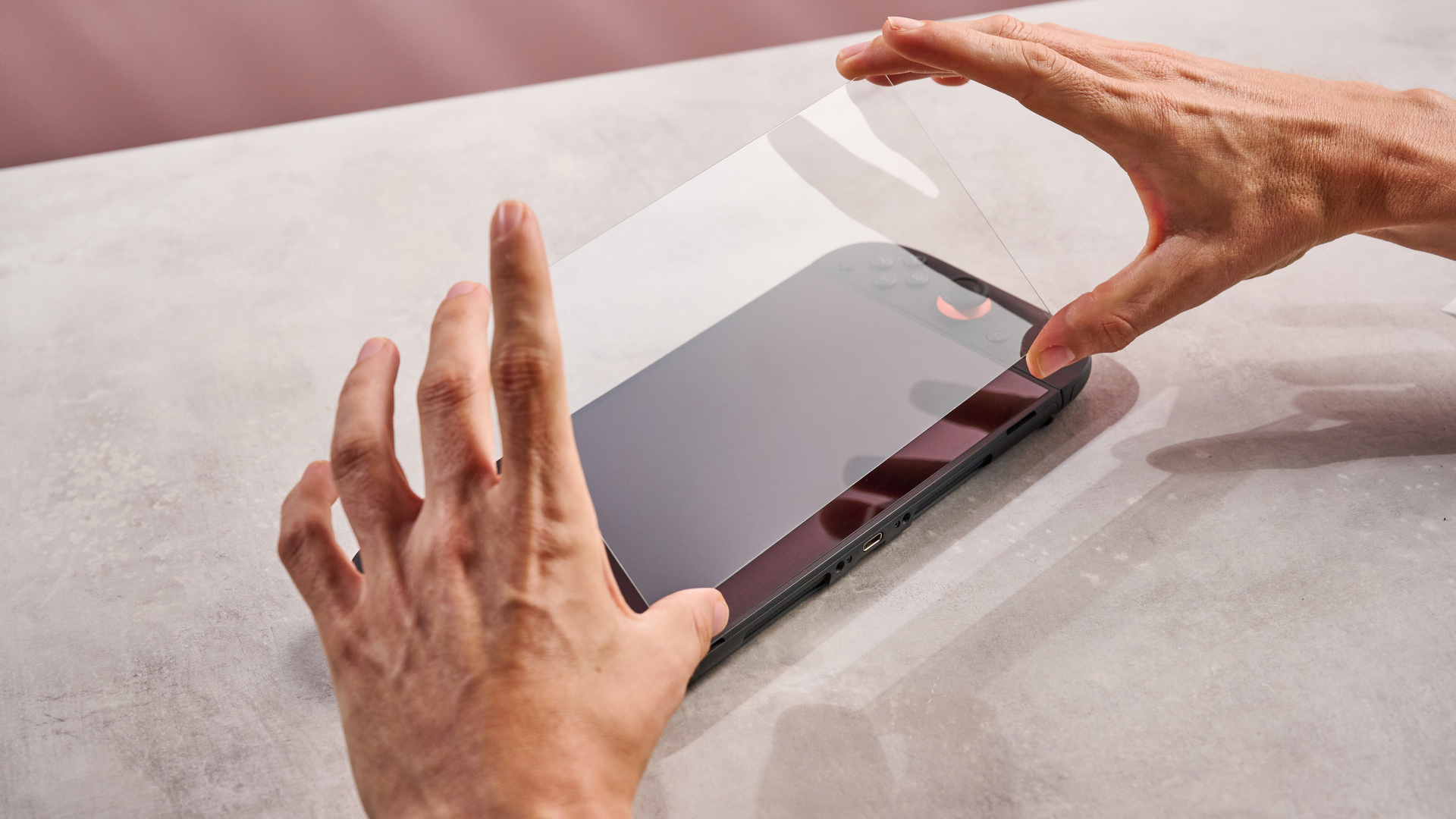 A man holding the Snakebyte Starter Kit S2 screen protector in position above the Nintendo Switch 2.