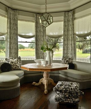 parlor with table and bench seats in bay window and patterned curtains