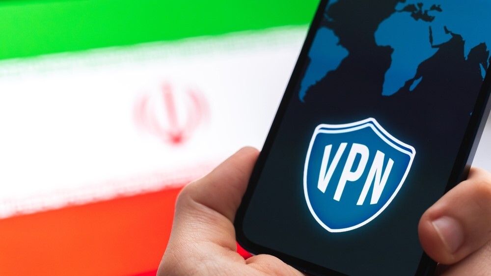 Hand holding a smartphone with a VPN logo on screen with an Iran&#039;s flag in the background