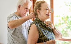 An older man puts a necklace on a woman who is smiling in a nice blouse. 