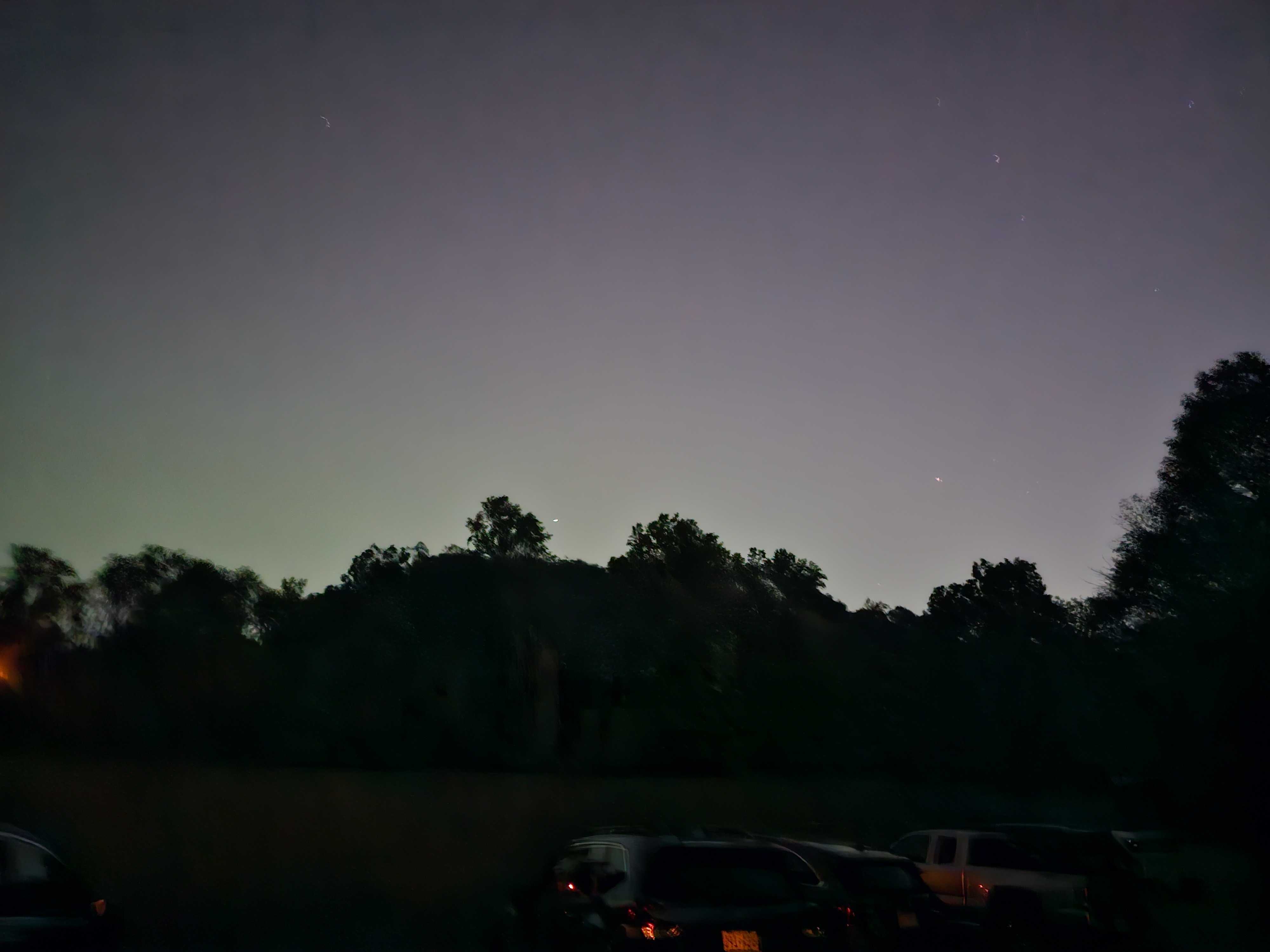 A dark purple sky with hints of green over dark trees