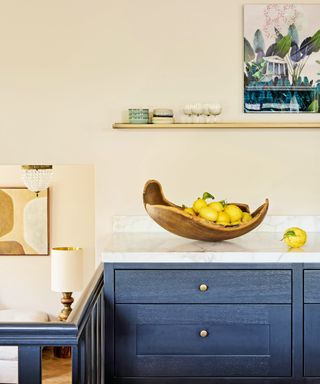kitchen with dark dark gray cabinets, marble worksurface, artwork, wooden shelf and wooden fruit bowl