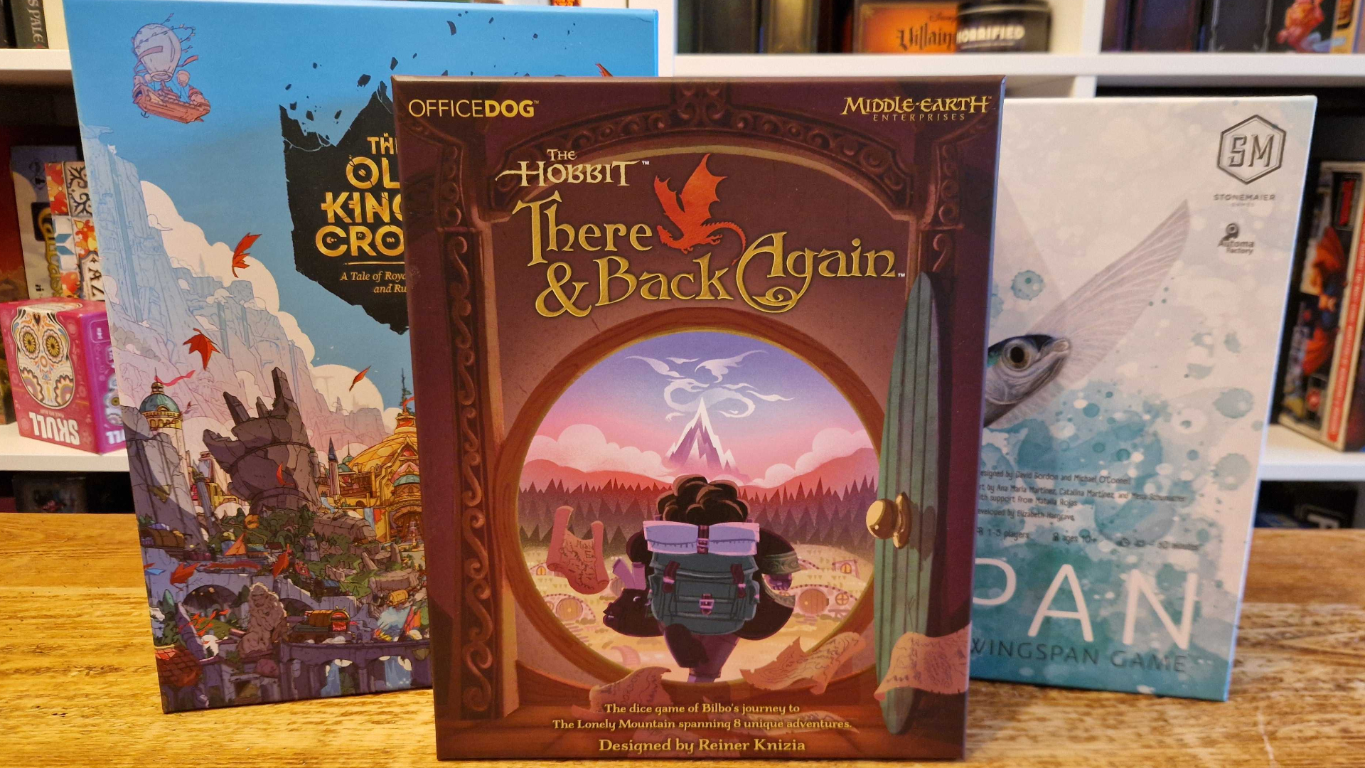The Old King's Crown, The Hobbit: There &amp; Back Again, and Finspan boxes on a wooden table in front of board game shelves