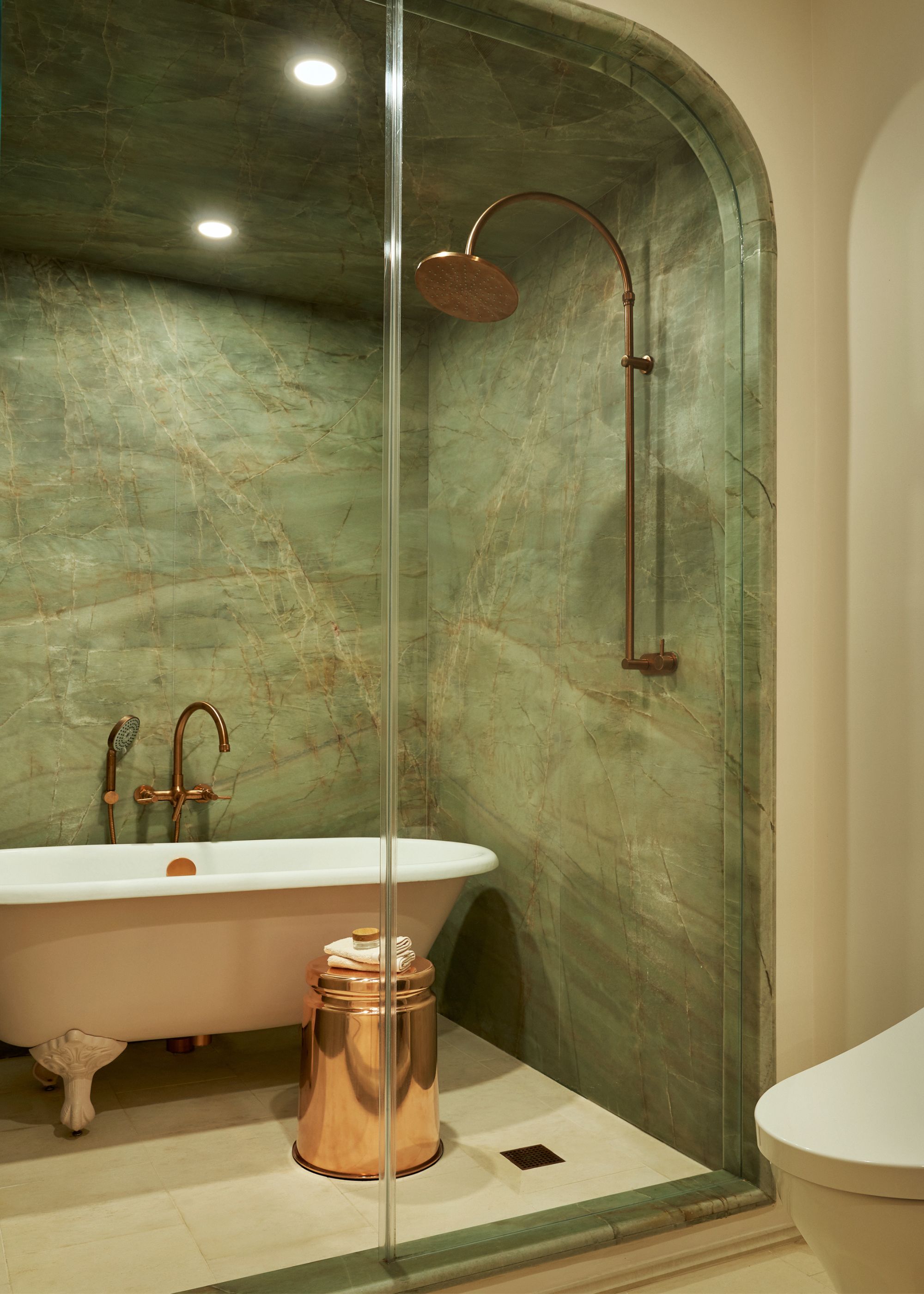 A green marble shower room with bronze fixtures, a free-standing bathtub, and a side table with a towel