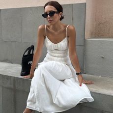Debora Rosa wearing a white sundress with black sunglasses and a black purse.