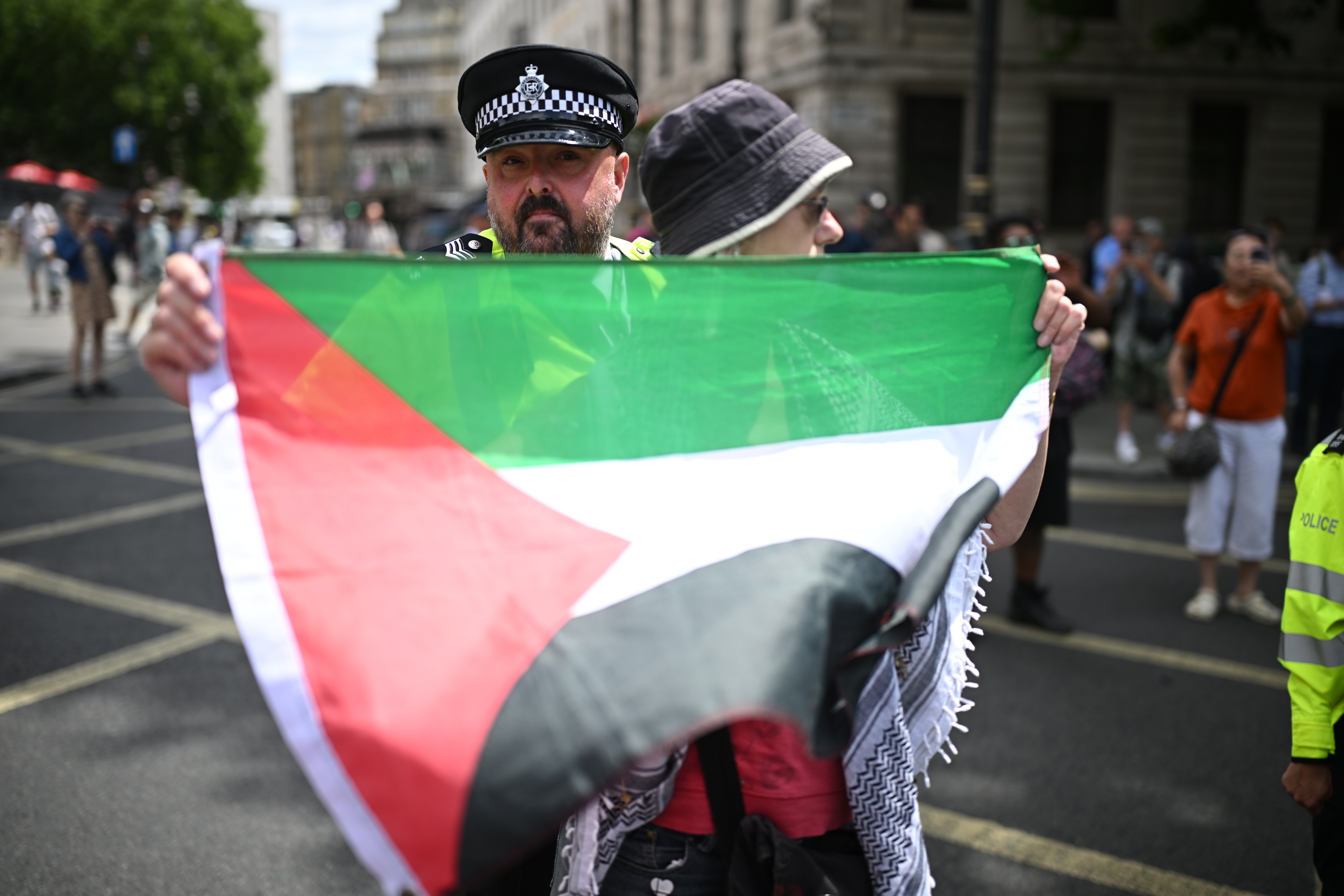 A protester holds a Palestinian flag in front of a police officer during a Palestine Action demonstration at Trafalgar Square on June 23, 2025 in London.