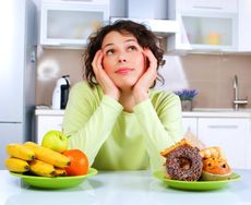 A woman thinks about whether to eat fruit, or donuts.