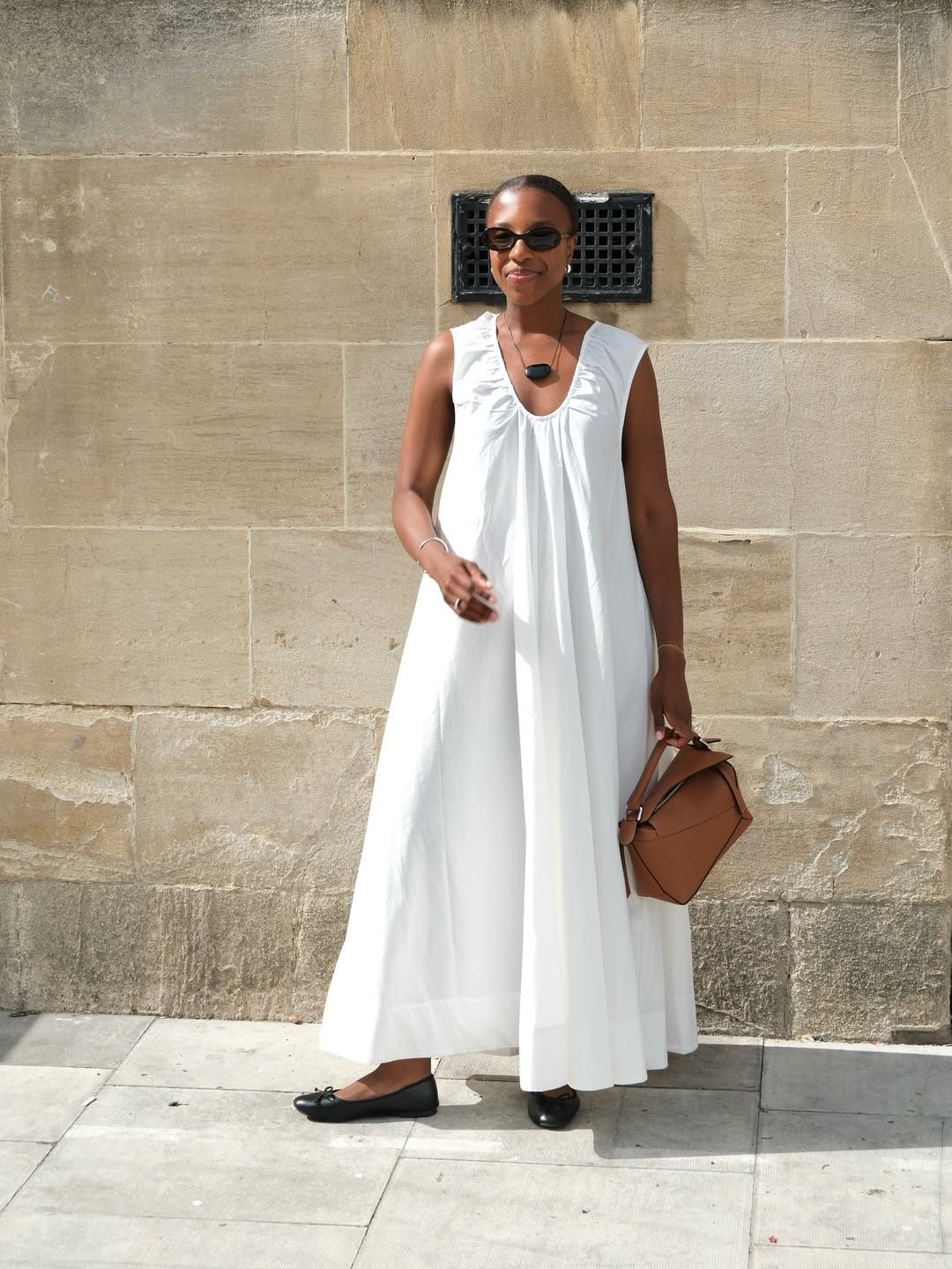 Woman wears white dress, brown bag and black ballet flats