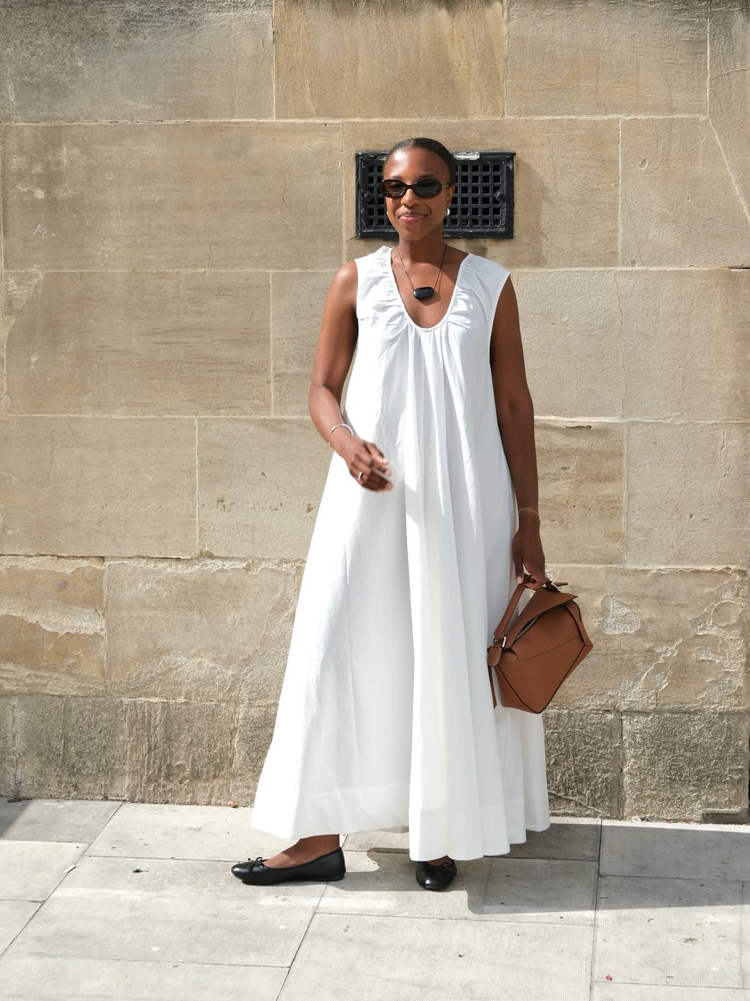 Woman wears white dress, brown bag and black ballet flats