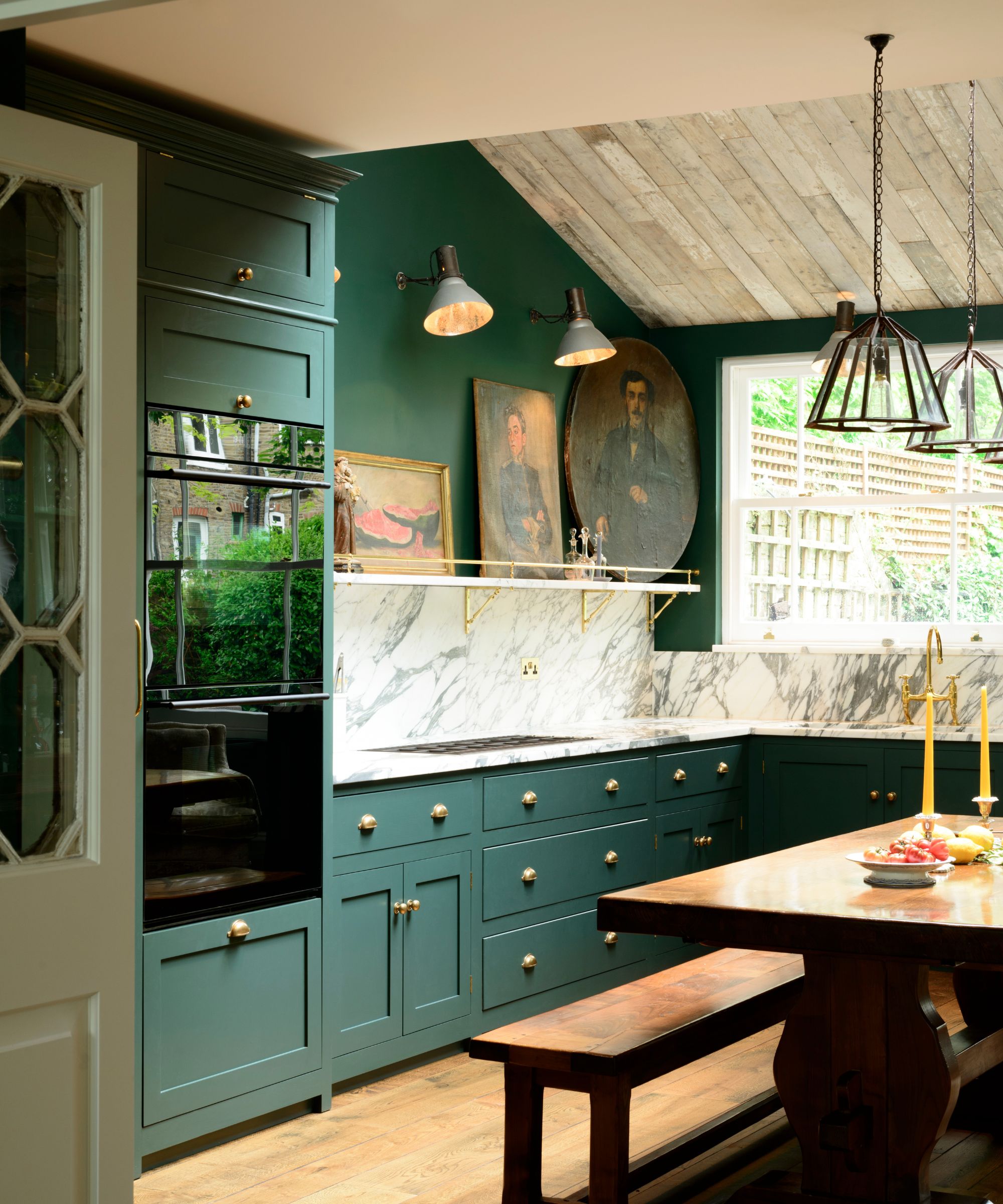modern rustic kitchen with dark green cabinets and walls, wood flooring and dining table with bench