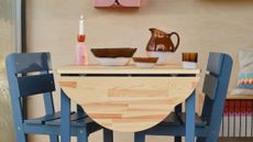 Breakfast table vignette featuring a wooden folded-leaf tabletop, blue chairs, and eclectic table decor