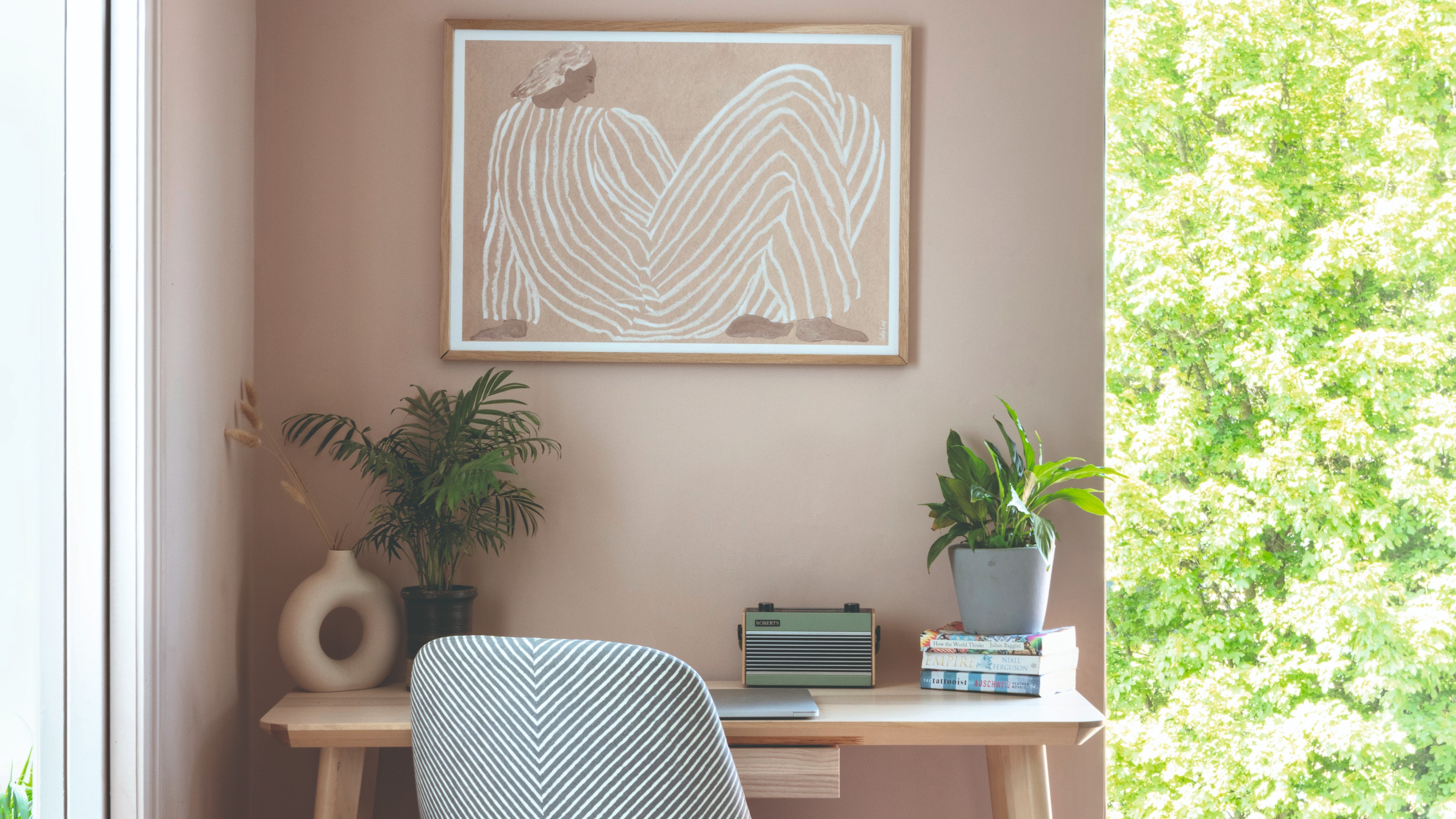 A pink-painted home office with a light wood desk and a tonal art print hanging on the wall