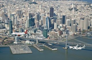 Virgin Galactic's SpaceShipTwo private spaceliner flies over San Francisco's Bay Area Bridge with the city as a backdrop while en route to San Francisco International Airport with the Virgin America aircraft