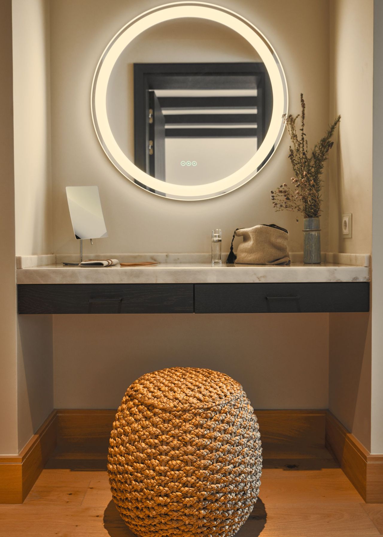 A large mirror sits above a table that holds a makeup bag and a plant. There is also a chair for guests to sit on when getting ready.
