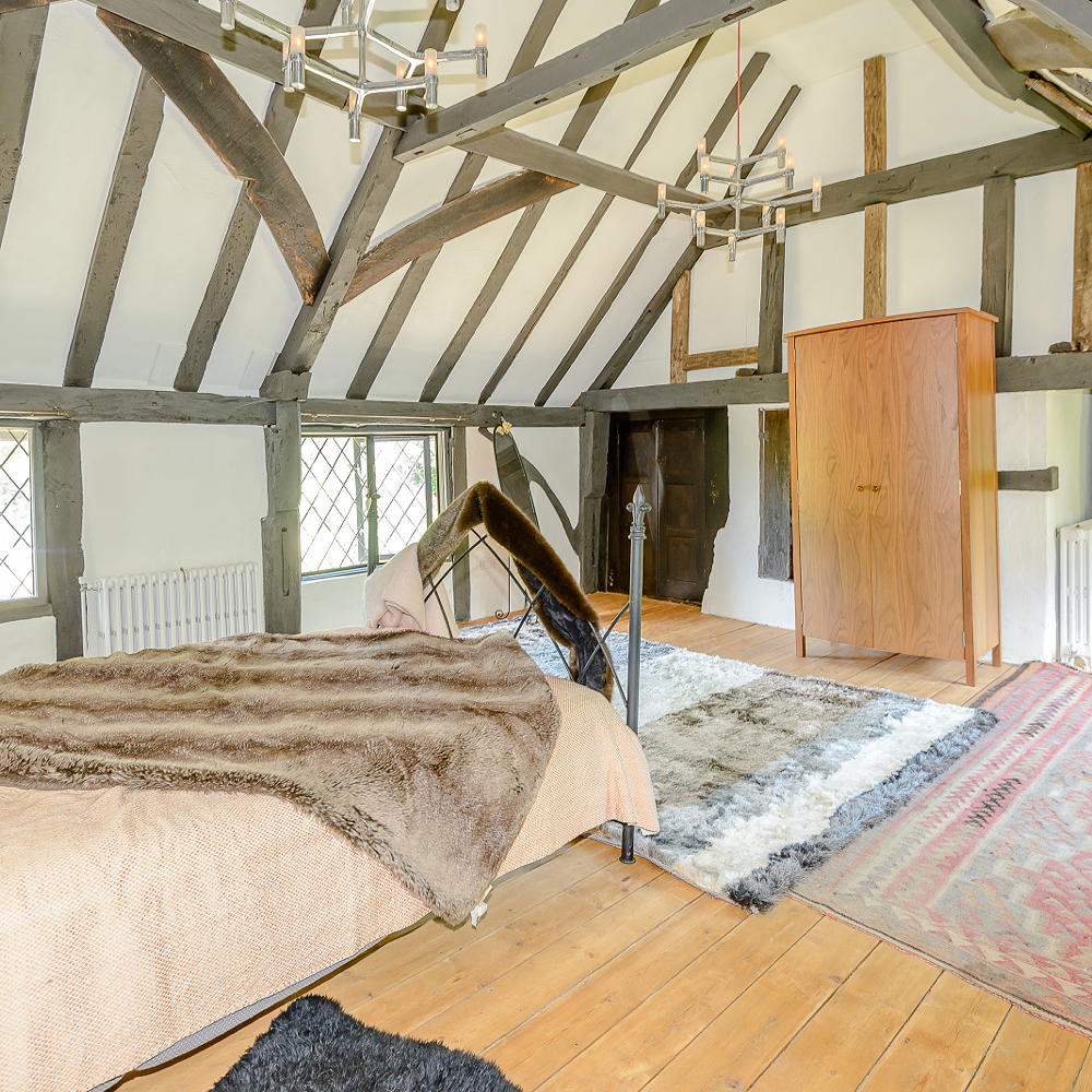 Bedroom with wooden flooring, various rugs, hanging light.