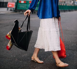 Model Xie Chaoyu wears a blue shirt, white skirt, jelly sandals, and a black origami swan bag during London Fashion Week September 2018 on September 16, 2018 in London, England.