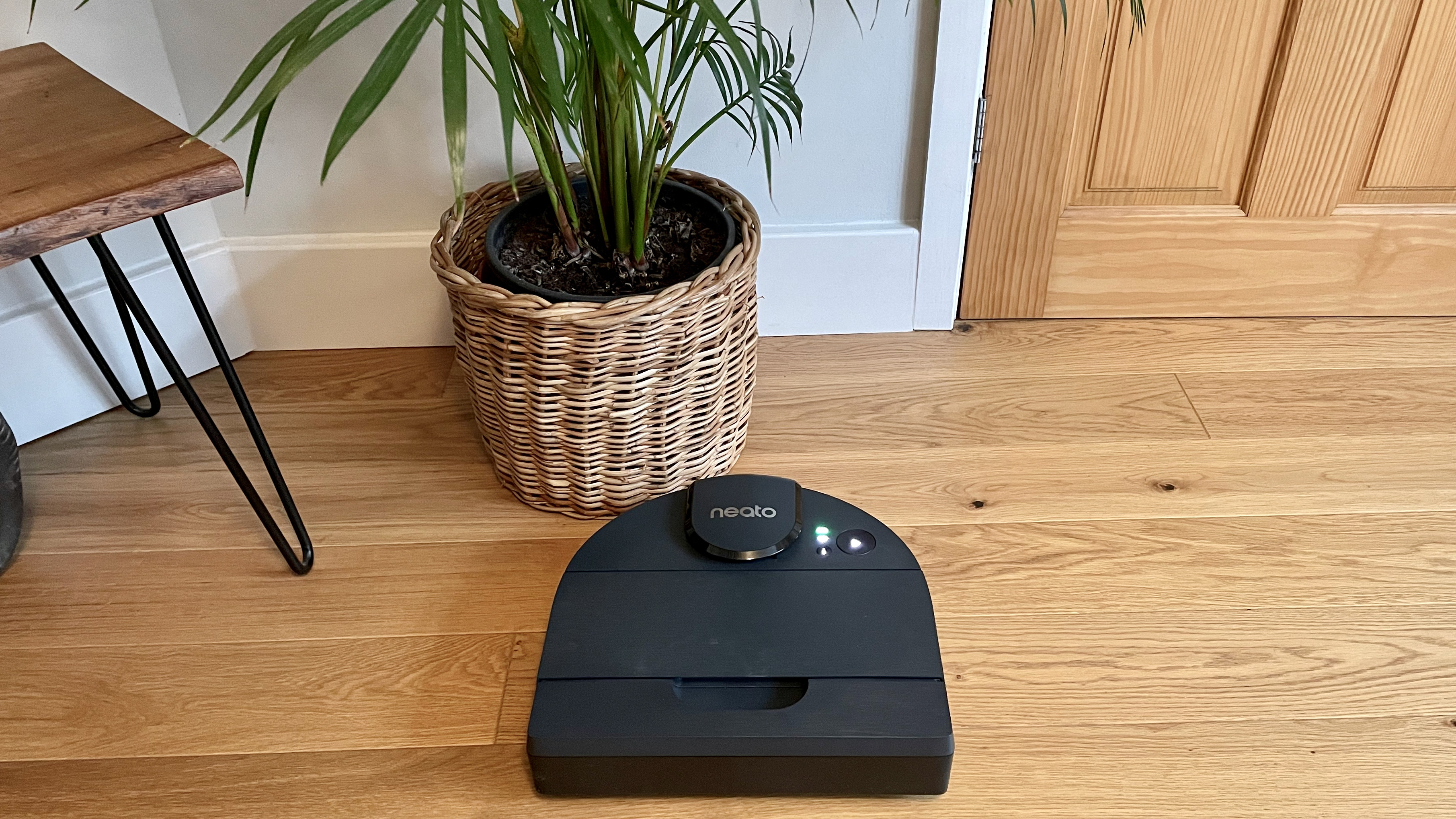 The Neato D8 next to a wicker plant pot cleaning a hard wood floor