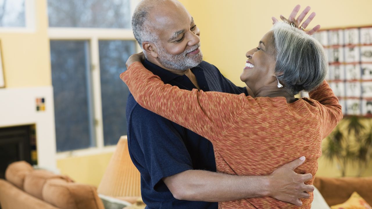 An older couple dance around their living room.