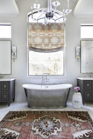 Silver bath with large window and twin grey sinks either side and warm coloured rug and curtain