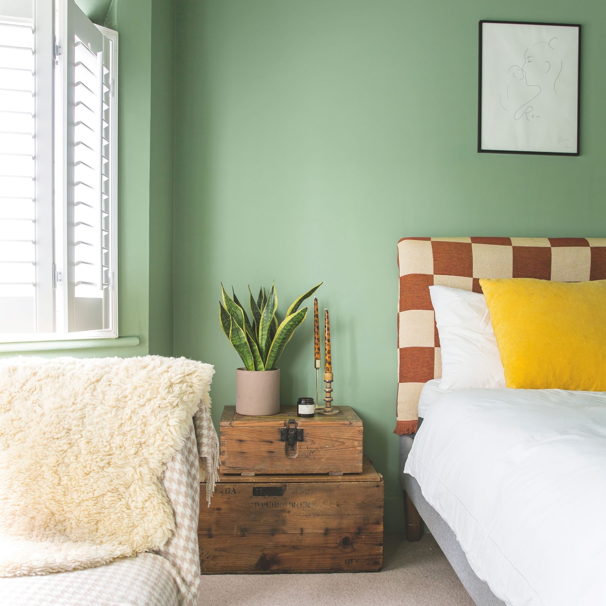 Green painted bedroom with a checkerboard headboard next to wooden storage crates with decor on it