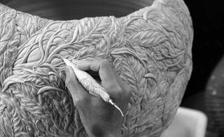 A close up of an artist carving an intricate design on a ceramic bowl