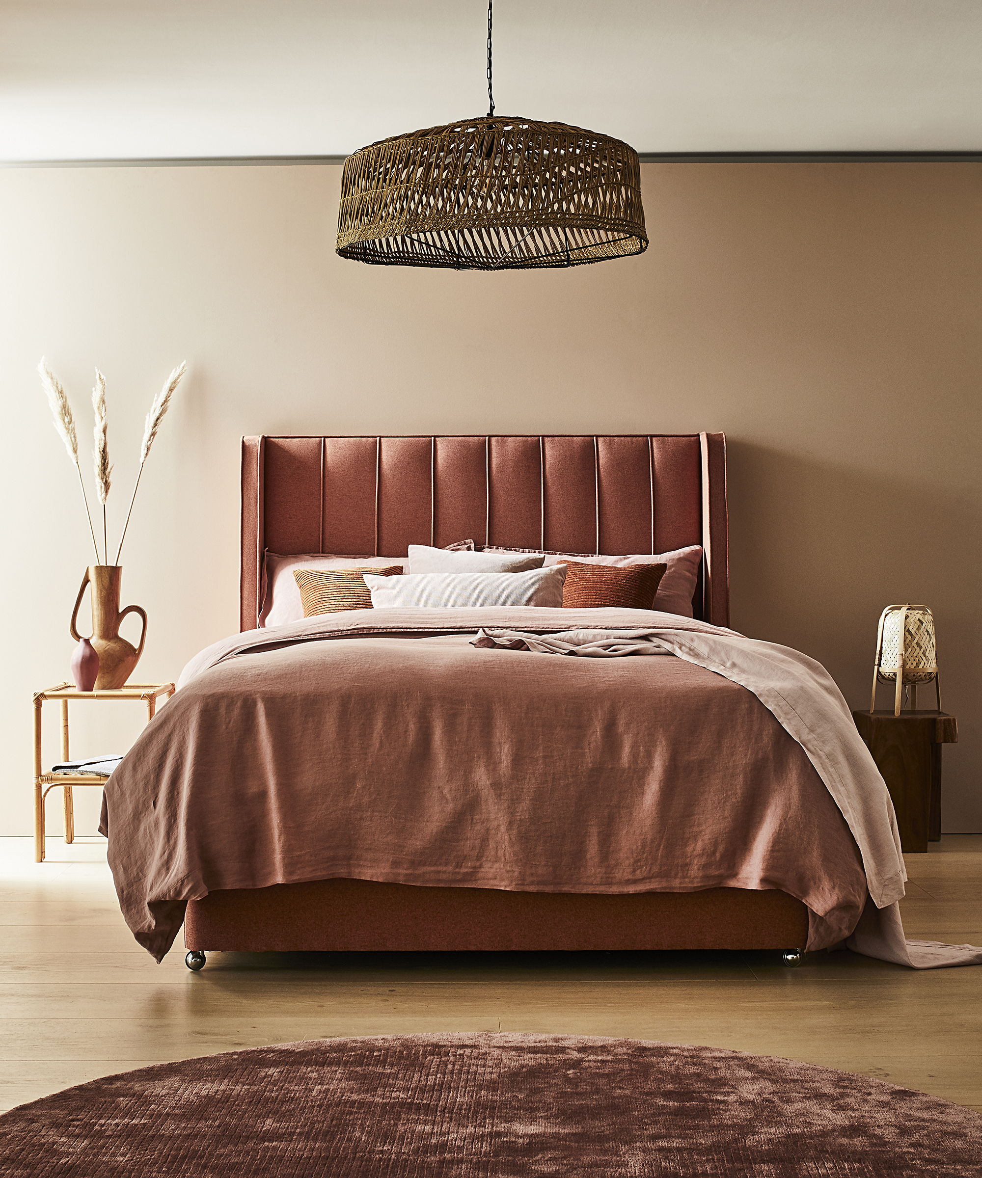 A pink bed in front of a pink wall with a rattan ceiling light